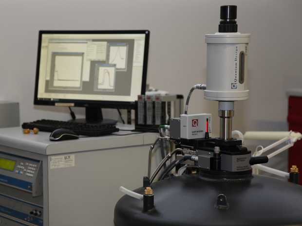 Laboratory device with measuring probe on round black housing in front of a monitor displaying graphs.