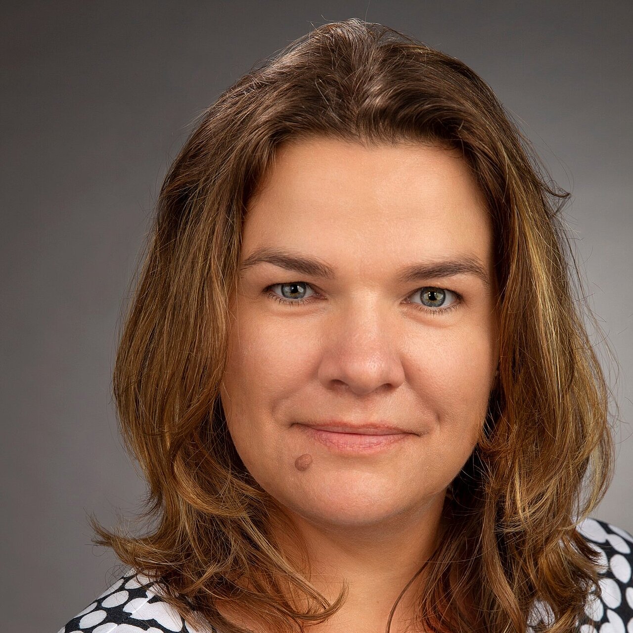 Portrait of Rita Taubert, a woman with shoulder-length brown hair looking at the camera wearing a black-and-white patterned top.