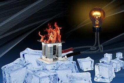 Ein metallenes Konstrukt steht mitten in einer Ansammlung aus Eiswürfeln. Über dem Konstrukt brennt eine Flamme. das Konstrukt ist mit einem Kabel verbunden, woran eine brennende Glühlampe angeschlossen ist.