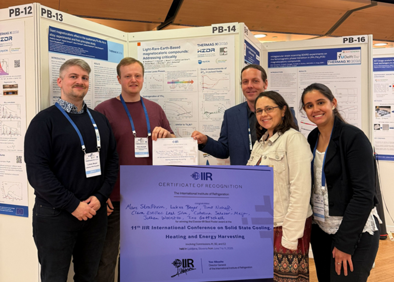 Group of five people standing in front of scientific posters at a conference holding a large certificate.