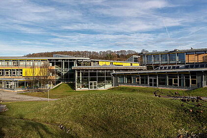 Wide-angle view of “Otto Lilienthal” Vocational School for Business in Freital, a modern school building with multiple connected wings, large windows, and a grassy area in the foreground.