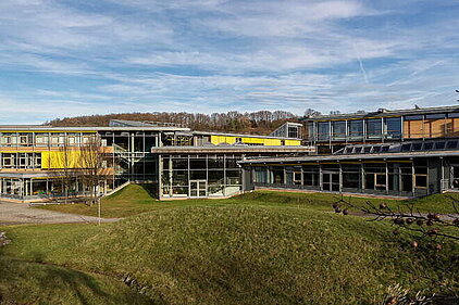 Das BSZ für Wirtschaft "Otto-Lilienthal" in Freital. Weitwinkelaufnahme des BSZ für Wirtschaft "Otto-Lilienthal" in Freital, ein modernen Schulgebäudes mit mehreren verbundenen Flügeln, großen Fenstern und einer Rasenfläche im Vordergrund.