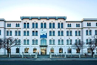 IHK Building - Front view of a multi-story white building with symmetrical windows and leafless trees in front.