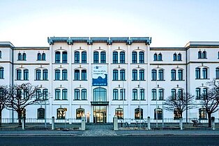 IHK Gebäude - Frontalansicht eines mehrstöckigen, weißen Gebäudes mit symmetrischer Fensteranordnung und kahlen Bäumen davor.