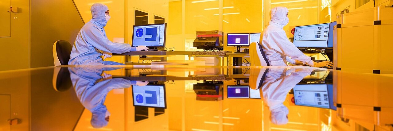 Zwei Wissenschaftler bei der Arbeit im Reinraum unter gelbem Licht.