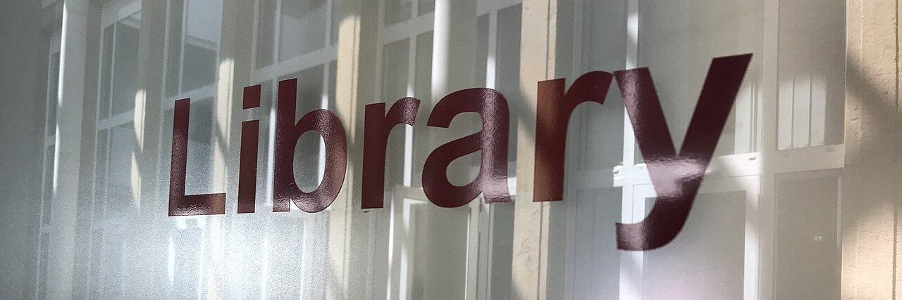 Türbeschriftung in den Buchstaben l i b r a r y an der Glastür zum Bibliothekseingang.