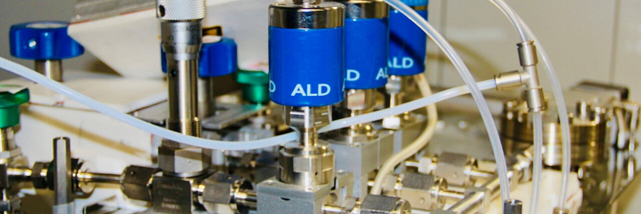 Close-up of a technical device with multiple blue cylinders connected by white tubes labeled 'ALD'