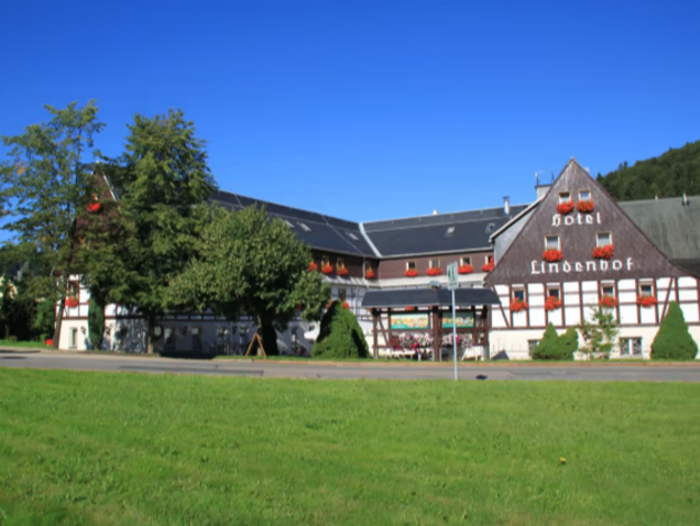Traditional half-timbered building with a sign reading 'hotel Lindenhof' under a clear blue sky and a green lawn in front.