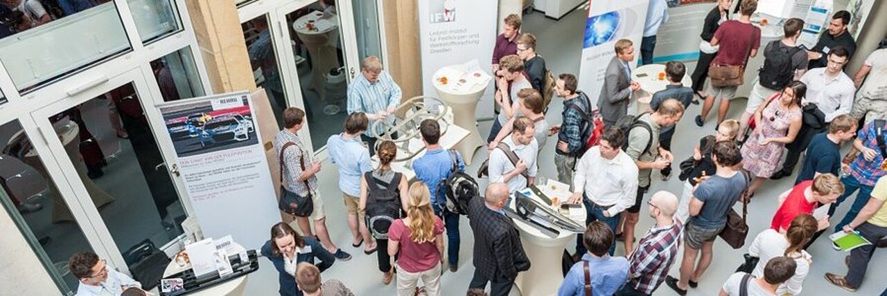 Viele Menschen sind im Atrium des IFW Dresden versammelt. Sie sind aus einem oberen Stockwerk fotografiert.