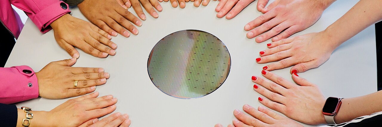 Multiple hands of different people placed in a circle on a white table with a round hole in the center.
