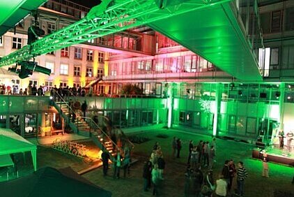 Innenhof des IF Gebäudekomplexes bei Nacht mit grüner Beleuchtung und mehreren Menschen, die sich in kleinen Gruppen aufhalten.