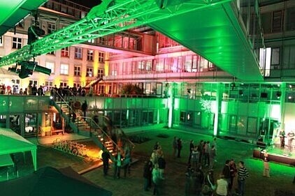 Courtyard of the IFW building complex at night illuminated in green with several people gathered in small groups.