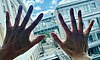 Two open hands held up against a window with a view of a modern building.