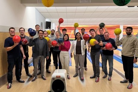 Members of the "Molecules To Materials"-Group standing on a bowling lane holding bowling balls above their heads.