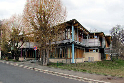 Meissen-Radebeul Vocational Training Center is a two-story school building with wooden cladding and large windows on a street in a suburban area with leafless trees in winter.