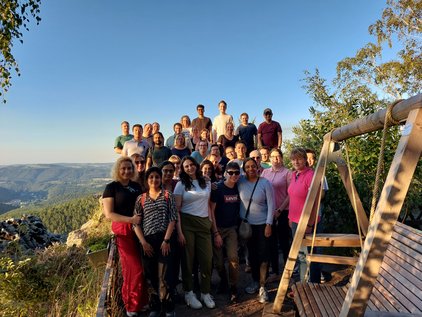 Group of people of IMC posing outdoors on a hill with a wooden swing and landscape in the background.