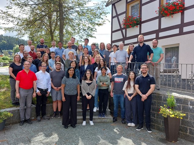 Group of people of IMC posing outdoors in front of a half-timbered building with flower boxes on the windows at Naturhotel Lindenhof in Holzhau