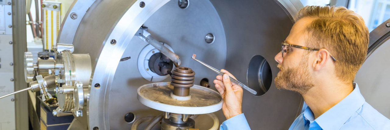 A scientist in a blue shirt is operating a casting machine containing a spiral-shaped metal component.