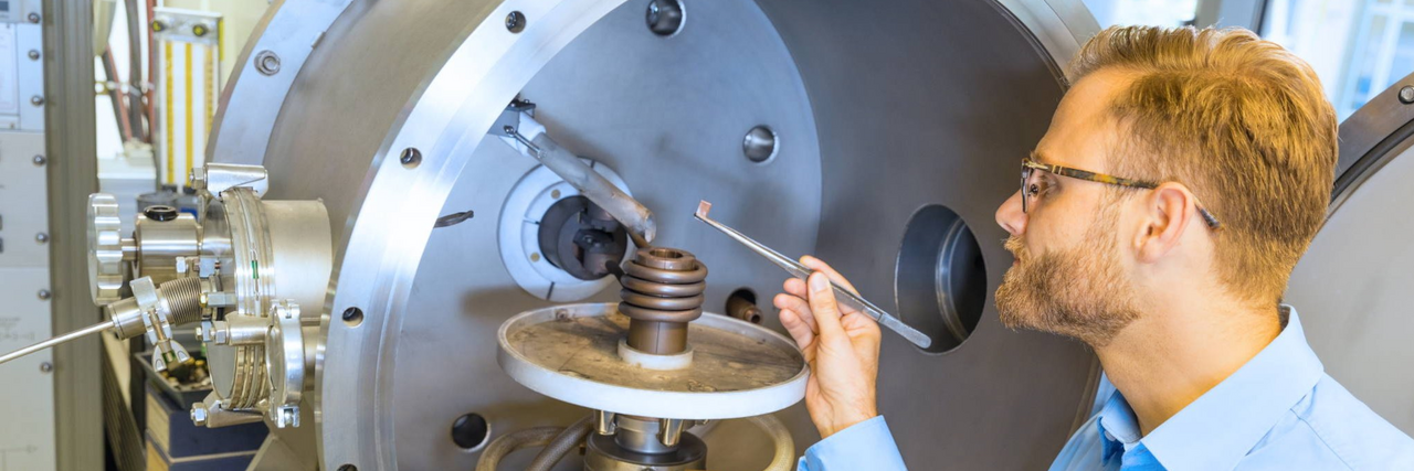 Wissenschaftler in blauem Hemd bedient eine Gießanlage mit spiralförmigem Metallteil im Inneren.