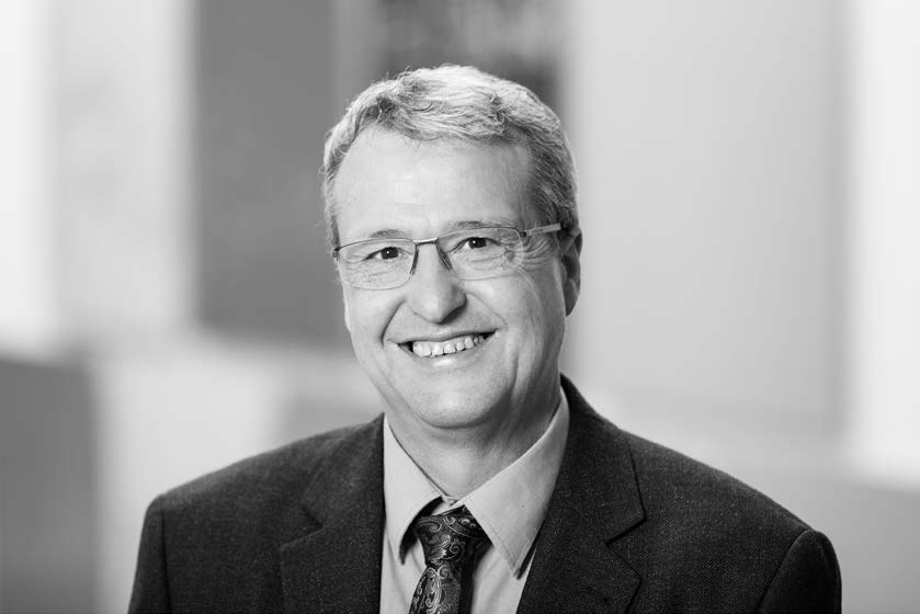 Portrait of Prof. Dr. Bernd Büchner, a smiling middle-aged man,  wearing glasses, suit, and tie against a blurred background.