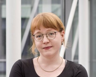 Haase with short blonde hair wearing a black top and silver necklace in front of a glass facade.