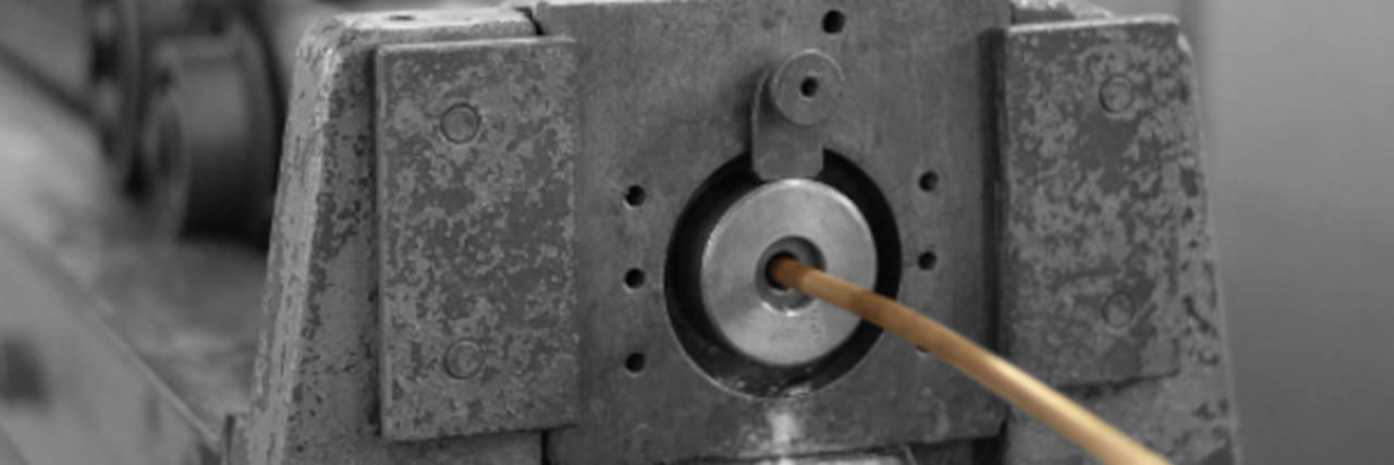 Nahaufnahme eines metallischen Maschinenteils mit einem dünnen Draht, der durch die Mitte gezogen wird.