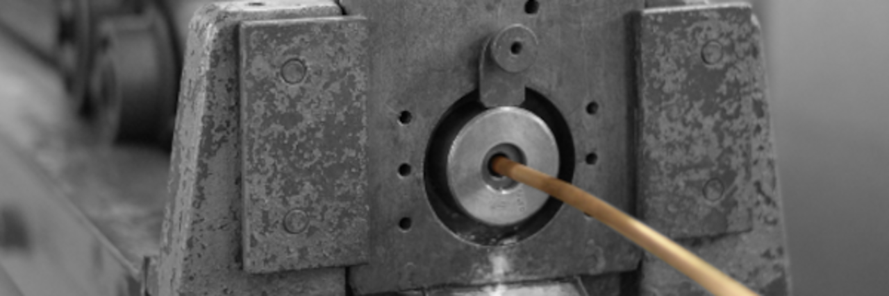 Close-up of a metallic machine part with a thin wire drawn through the center.