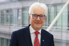 Portrait of theoretical physicist Prof. Vladimir Fomin at IFW Dresden in front of a modern glass-and-steel interior. He is wearing a dark suit, a white dress shirt, and a red striped tie.