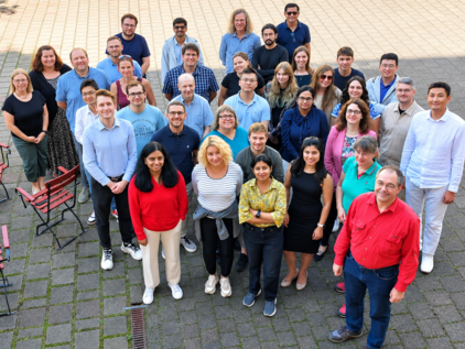group picture from IMC at 2025 retreat (c)Präßler-Wüstling at IMC/IFW Group of diverse adults from IMC standing outdoors on a paved area looking up at the camera.