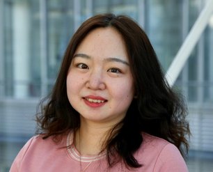 Dr. Yue Dong with short blonde hair wearing a black top and silver necklace in front of a glass facade.
