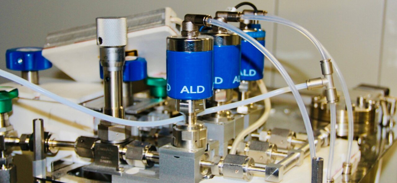 Close-up of a technical device with multiple blue cylinders connected by white tubes labeled 'ALD'