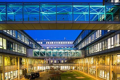 IFW Dresden Blick in den Innenhof des IFW-Gebäudes Dresden mit beleuchteten Glasbrücken und modernen Bürogebäuden bei Abenddämmerung.