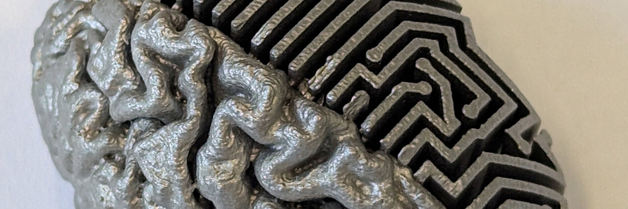 Metallisches, im 3D-Druck hergestelltes Gehirnmodell, dessen eine Hälfte realistische Hirnwindungen und dessen andere Hälfte ein abstraktes, labyrinthartiges geometrisches Muster aufweist.
