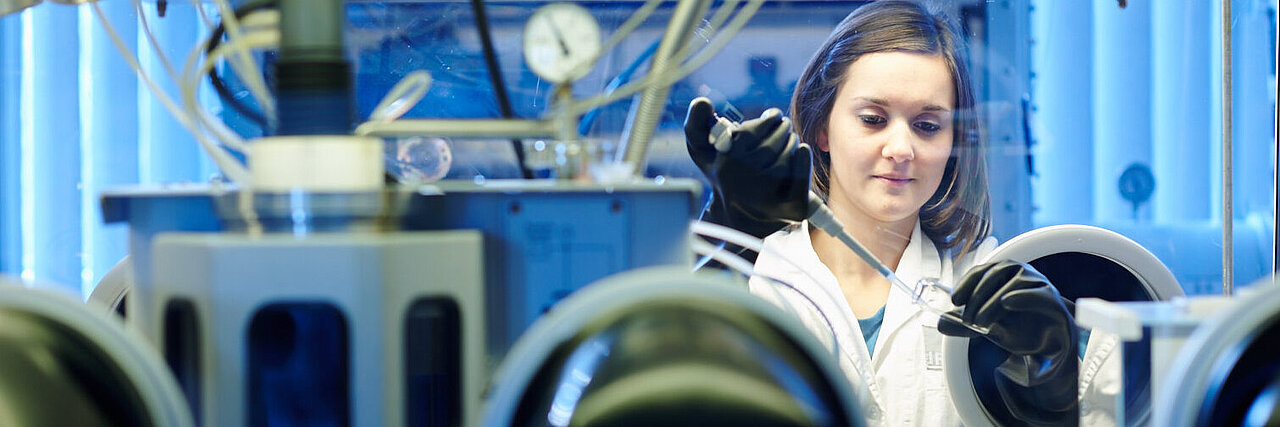 Eine junge Frau arbeitet an einer Glovebox im Chemielabor des IFW Dresden.
