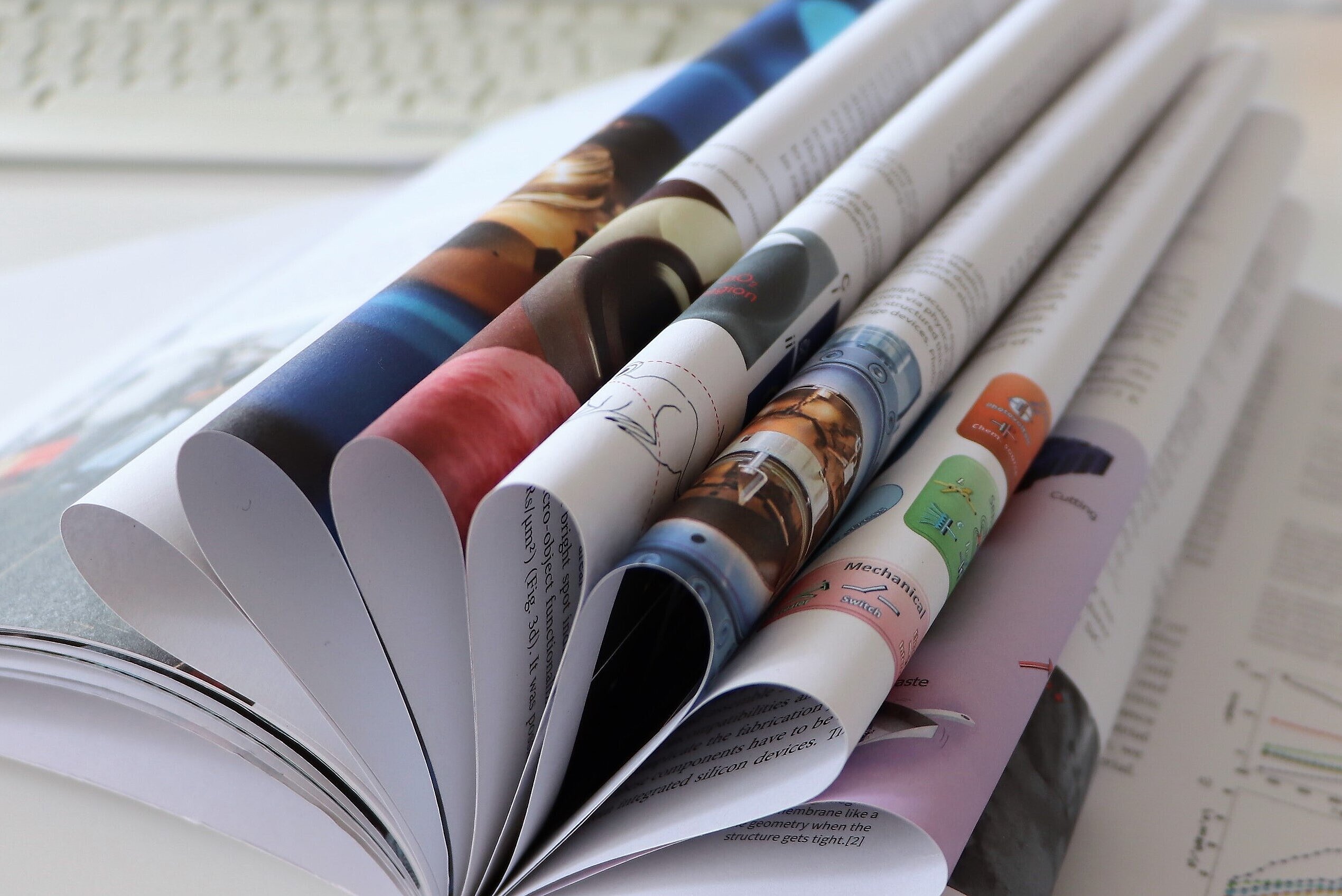 An open annual report with several pages turned, lying on a white desk with a keyboard in the background.