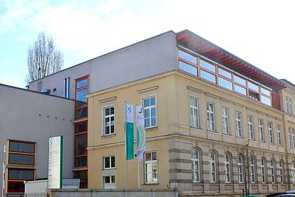 Building complex with historic multi-story sandstone building and modern annex featuring SBG logo in Dresden.
