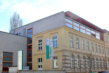 SBG in Dresden. Zweigeschossiges Schulgebäude mit Holzverkleidung und großen Fenstern an einer Straße in einer Vorstadt mit kahlen Bäumen im Winter.