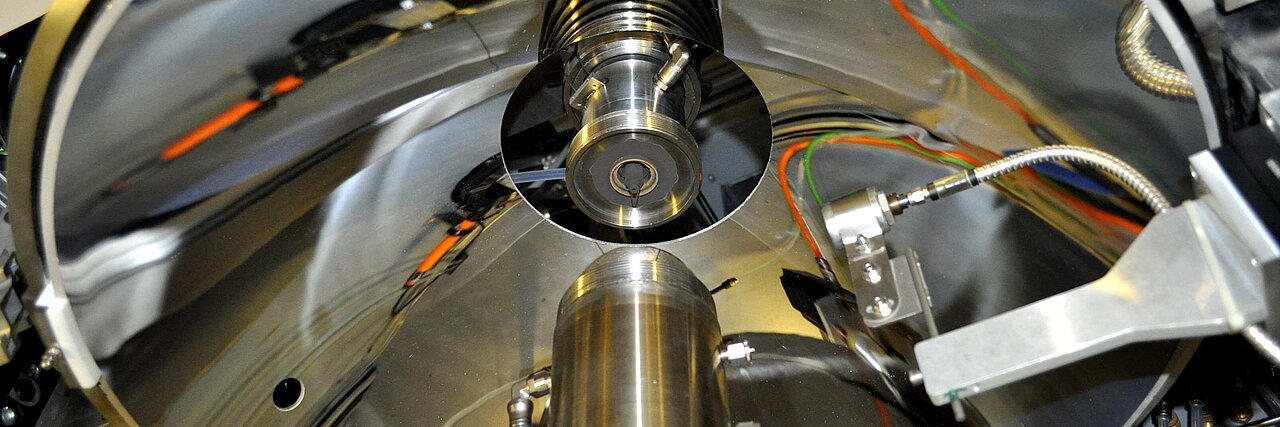 Concave mirror in a single crystal growth facility with reflective round metal surface and attached cables and components.