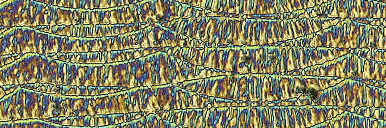 Optical micrograph shows close-up of a metallic microstructure with wavy lines and elongated grains.