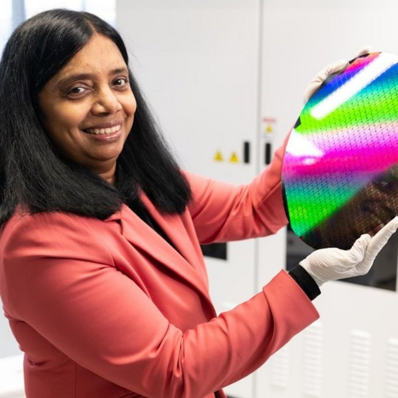 Dr. Anjana Devi wearing white gloves holding a reflective semiconductor wafer with a rainbow pattern.