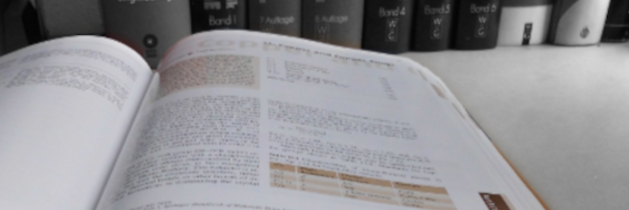 Open publication showing text and tables in front of a bookshelf with more books. 