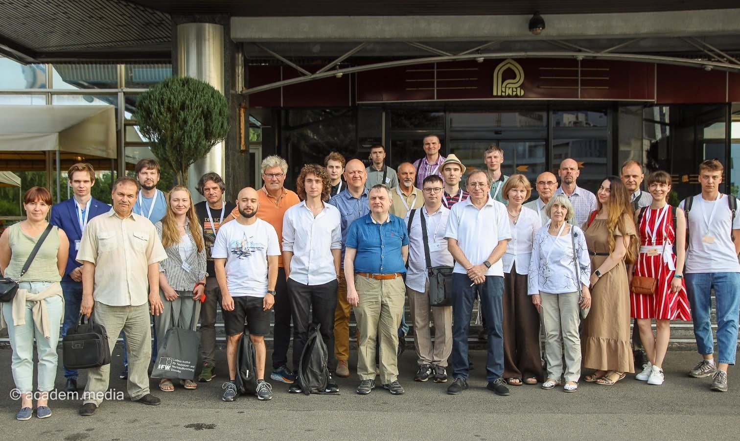 Die Teilnehmenden der Konferenz haben sich zu einem Gruppenbild aufgestellt. 27 Personen stehen in zwei Reihen vor einem Gebäude.