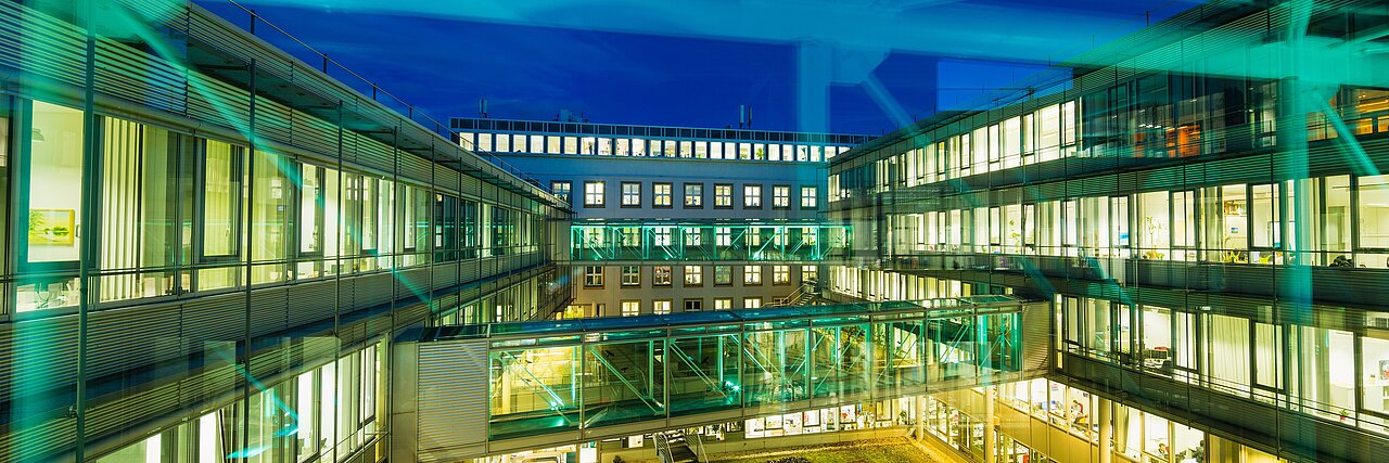 Courtyard of the modern part of the IFW building in Dresden with glass bridge and illuminated windows at night.