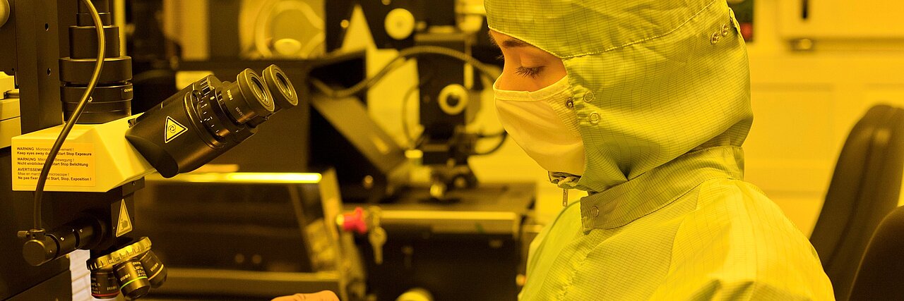 Person wearing protective clothing and mask working at a microscope in a laboratory at the IFW Dresden.