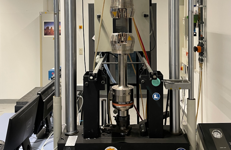 Instron 8502 testing machine with a cylindrical test specimen clamped inside in a laboratory room.