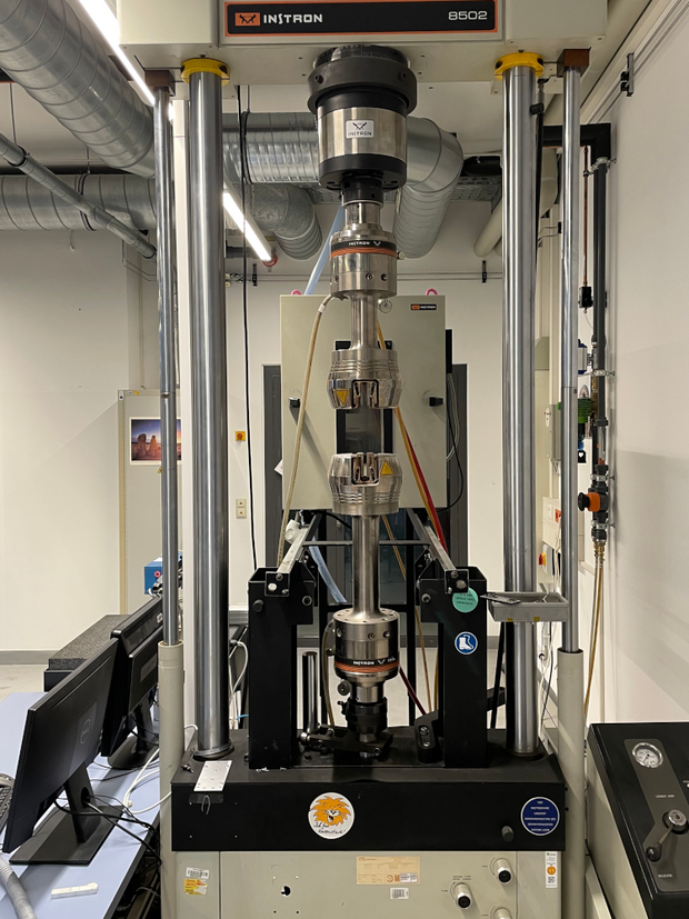 Instron 8502 testing machine with a cylindrical test specimen clamped inside in a laboratory room.
