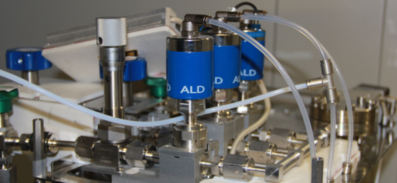 Close-up of a technical device with multiple blue cylinders connected by white tubes labeled 'ALD'