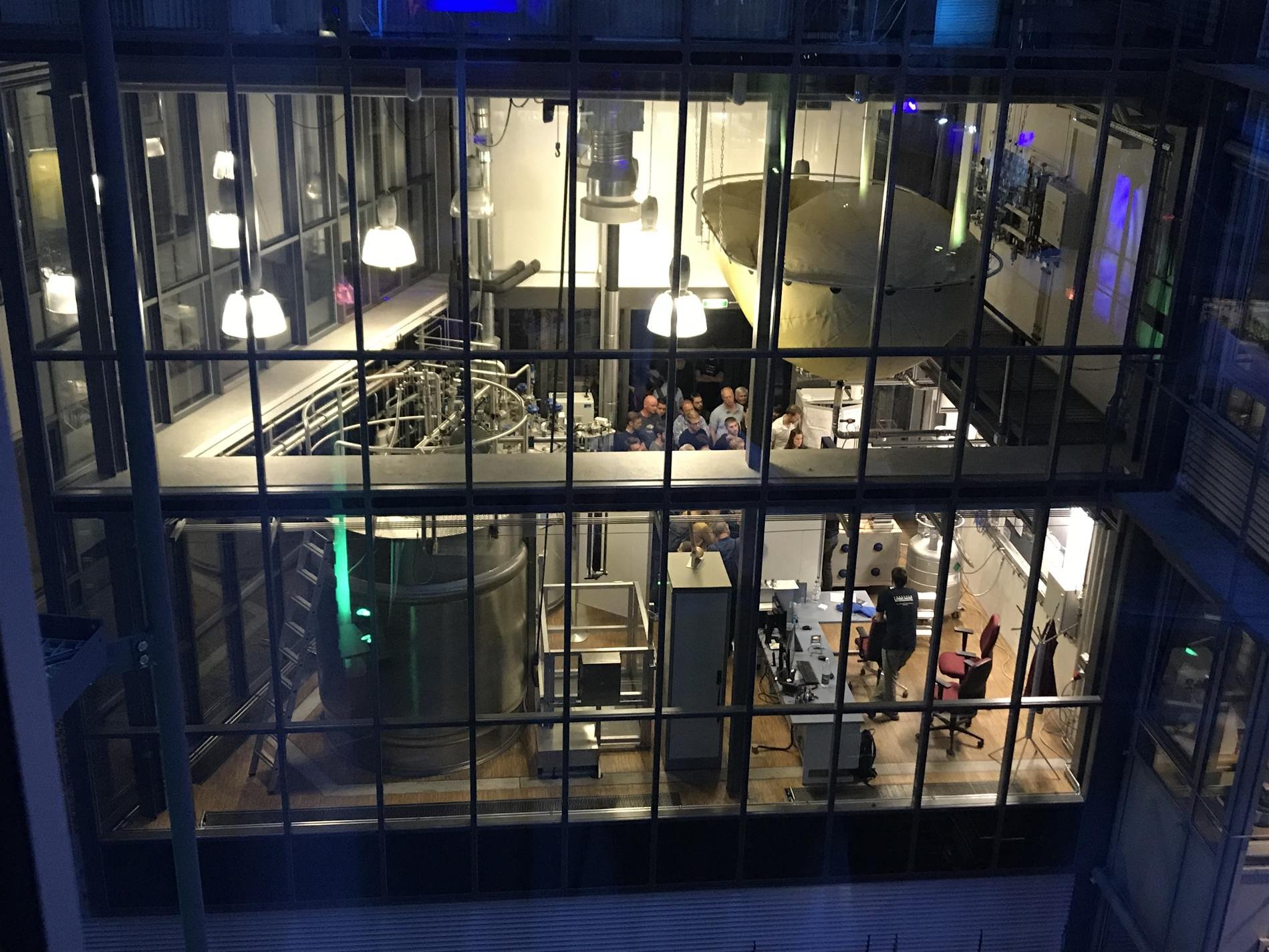 View through a large window into a room with several people, technical equipment, and large containers in a scientific building at IFW Dresden.