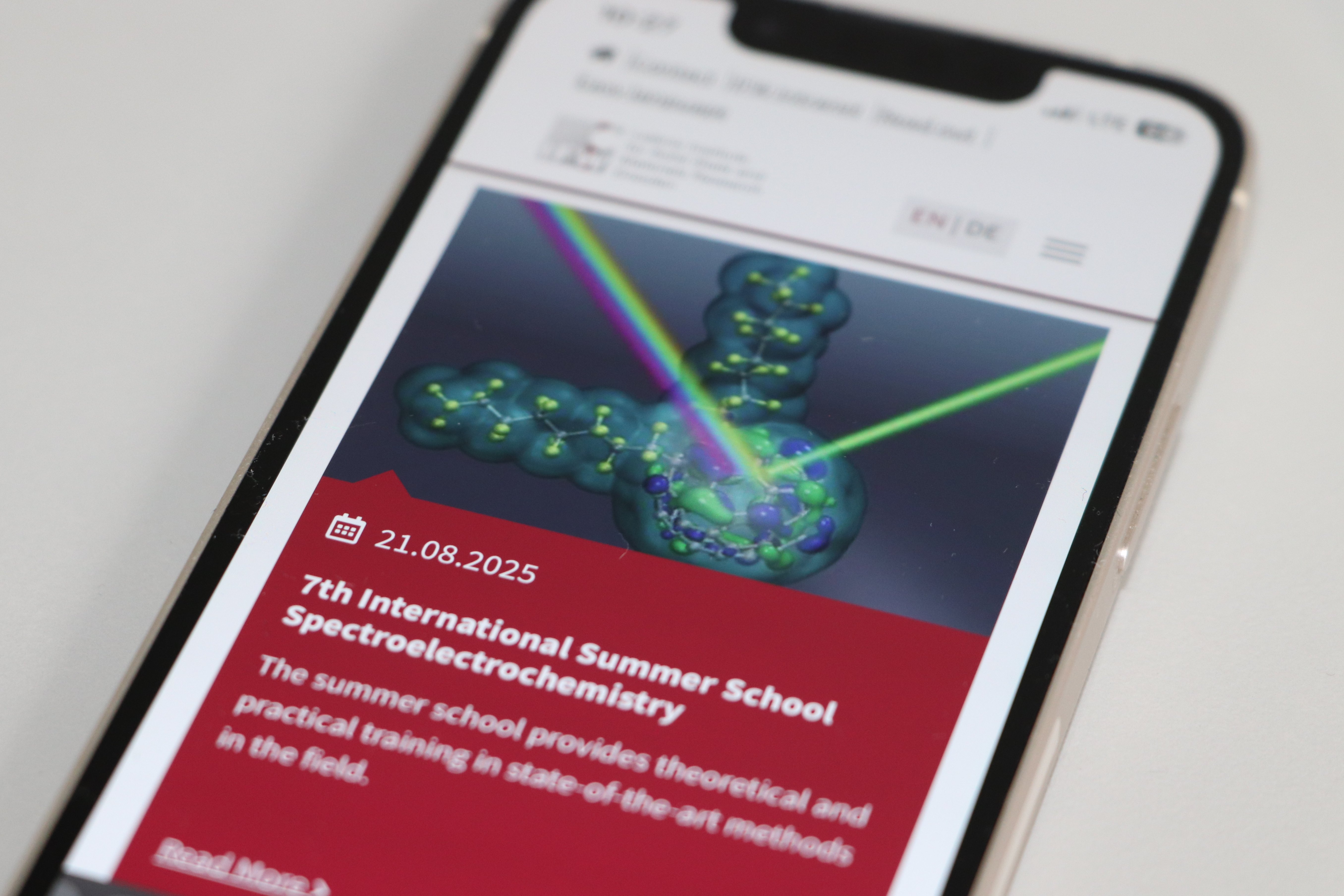 Smartphone displaying announcement for the 7th International Summer School on Spectroelectrochemistry with graphic of a molecule and light beams.