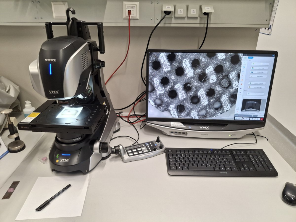 Microscope with connected monitor displaying a magnified black-and-white image of round structures.